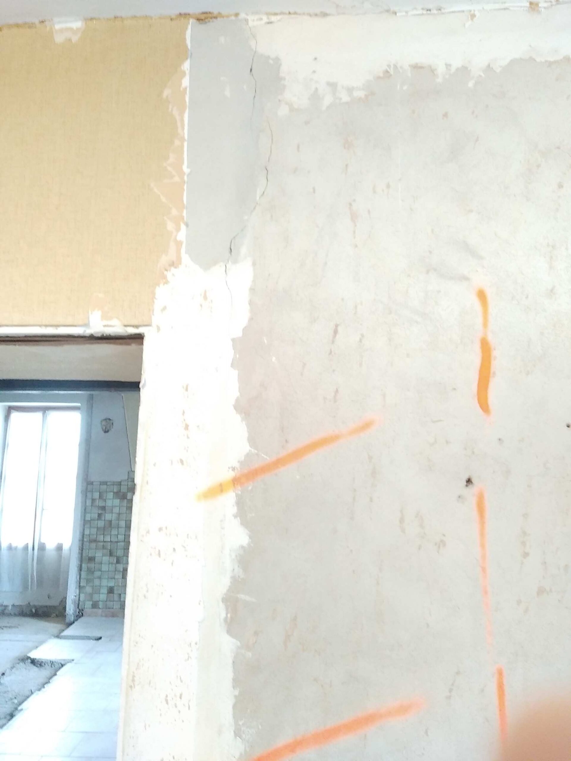 Rénovation intérieure: mur avec papier peint jaune décollé, plâtre blanc fissuré et lignes de marquage orange, pièce en travaux.