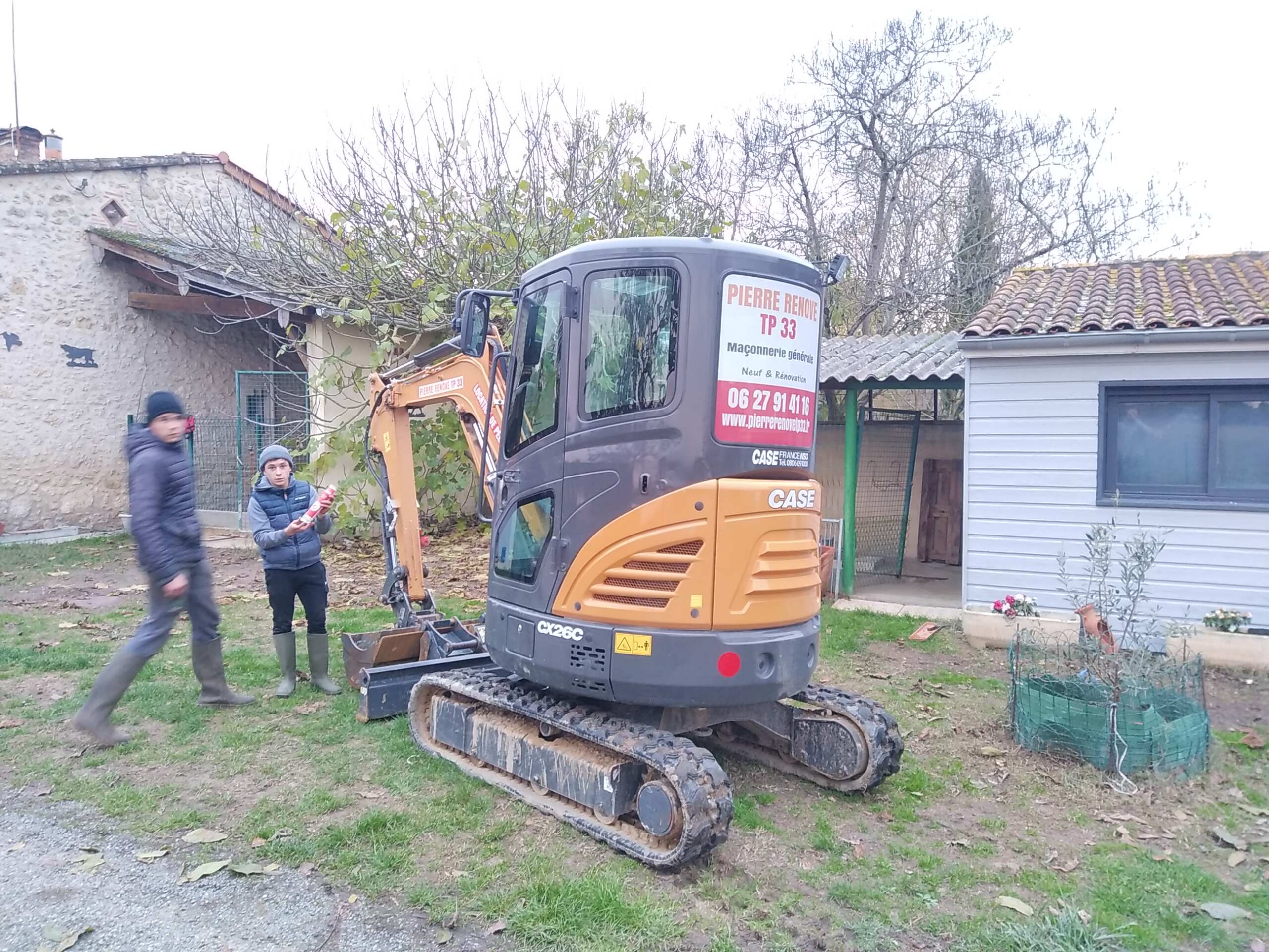 Mini-pelle CASE CX26C de PIERRE RENOVE TP 33 (Maçonnerie générale, 0627914116) avec deux jeunes garçons dans un jardin. L'un tient une bombe.