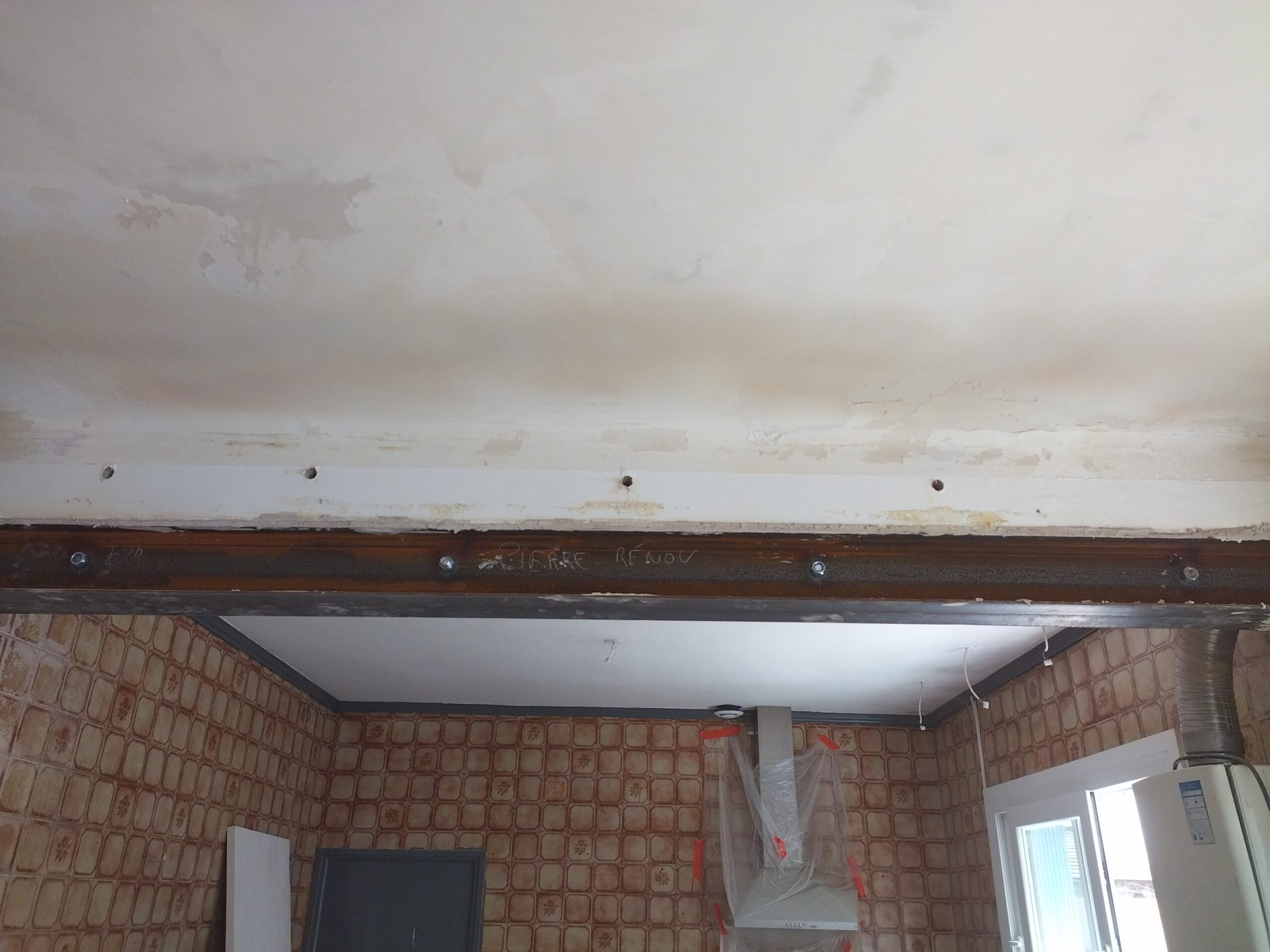 Plafond avec dégâts des eaux et poutre métallique "PIERRE - RENOV" dans une cuisine carrelée en rénovation, avec hotte et appareils.