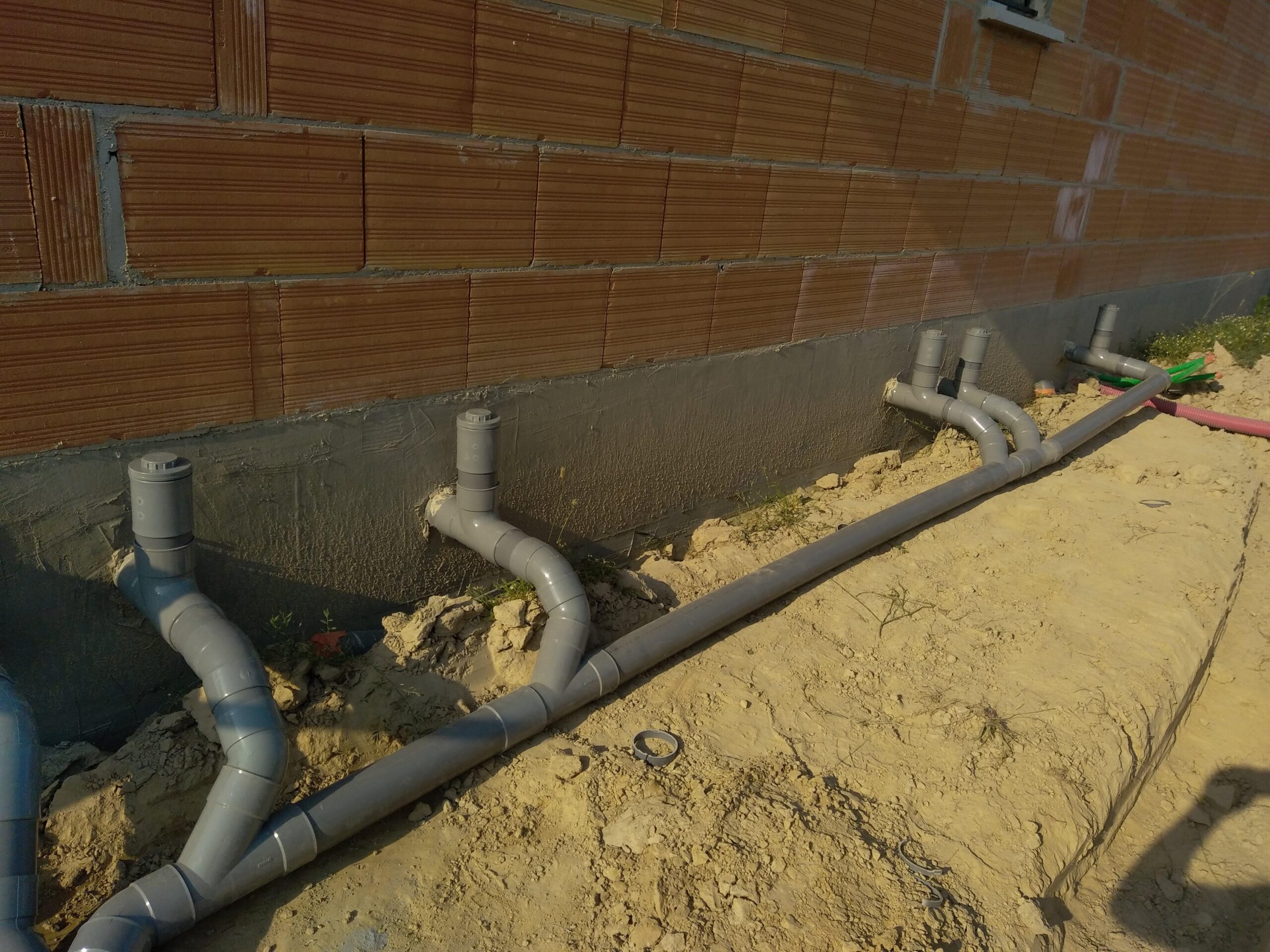 Tuyaux de drainage en PVC gris sortant de la fondation d'un mur en briques. Un système d'évacuation enterré en cours d'installation.