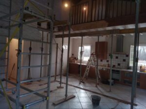 Intérieur de maison en pleine rénovation avec étaiement, échafaudage, cuisine équipée, et mezzanine sous des poutres soutenues.