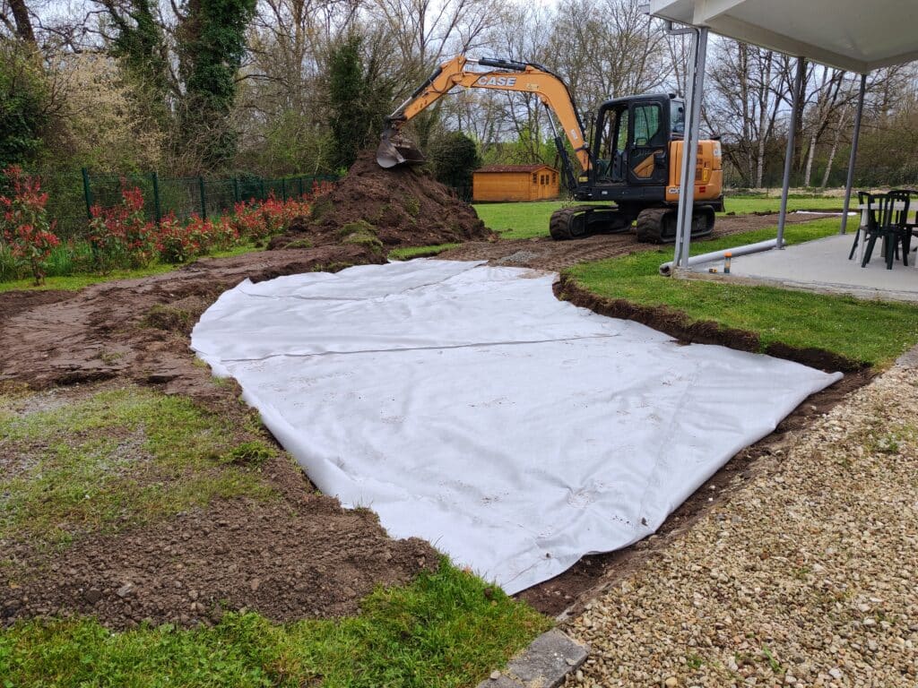 Excavatrice CASE préparant un chantier avec une bâche géotextile blanche "HIRETEC Polofelt TS-30" posée au sol.