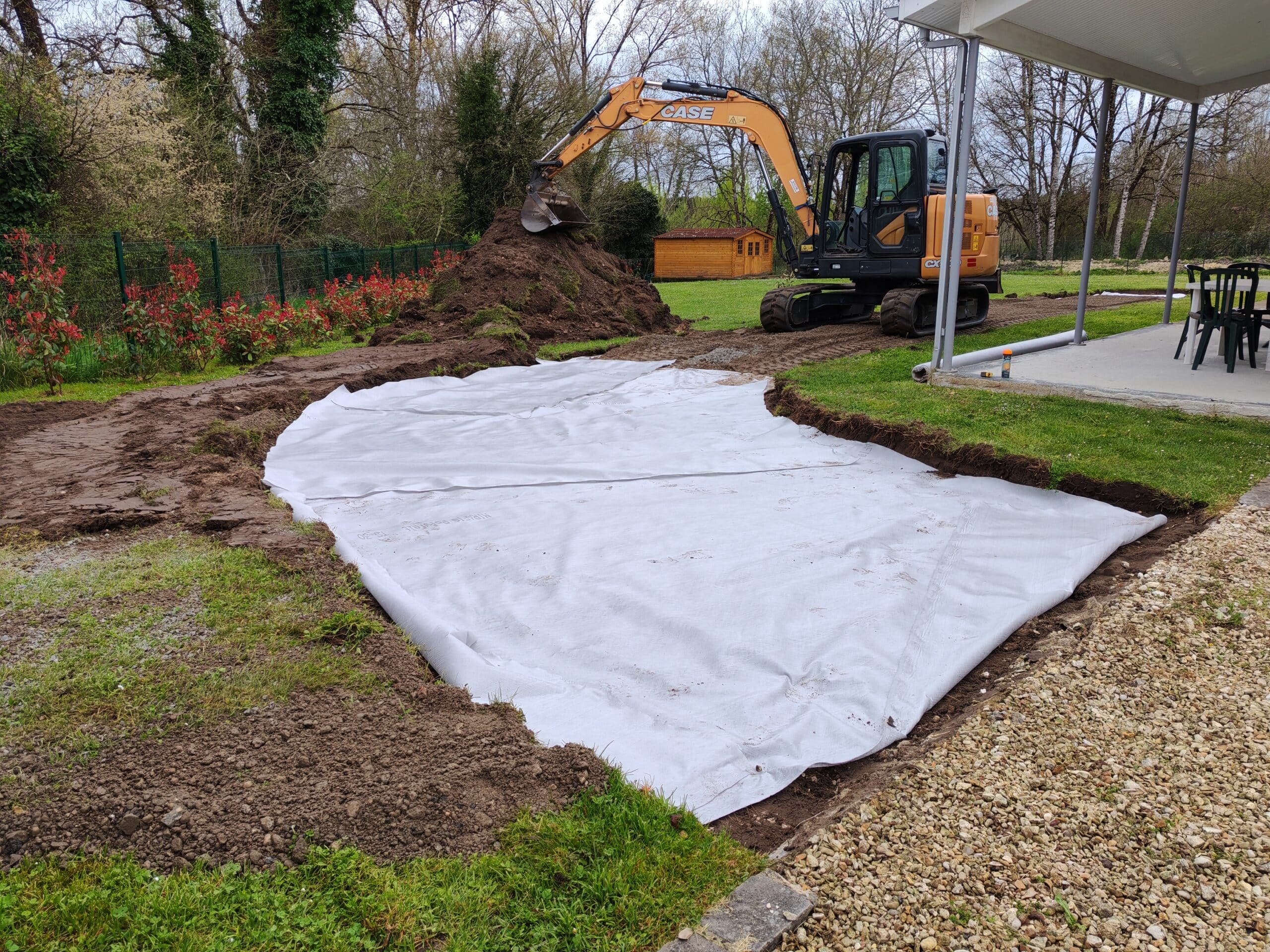 Excavatrice CASE préparant un chantier avec une bâche géotextile blanche "HIRETEC Polofelt TS-30" posée au sol.