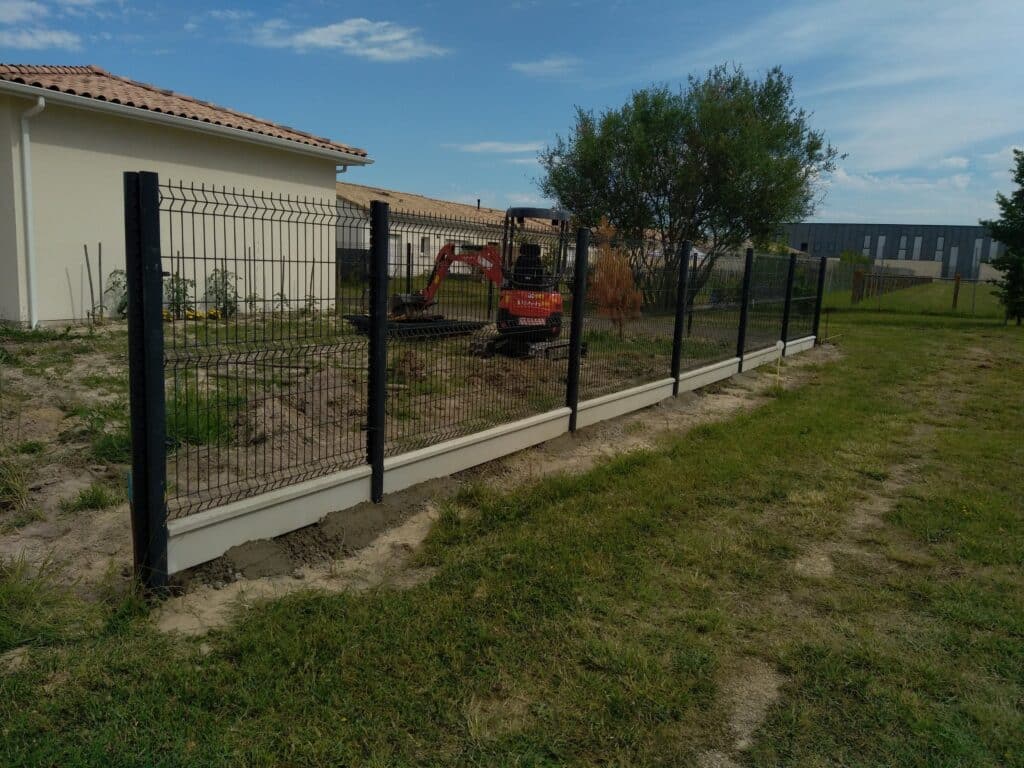 Pose de Clôture Rigide Noire avec Soubassement Béton Pose d'une clôture rigide noire avec soubassement béton dans un jardin en cours d'aménagement.