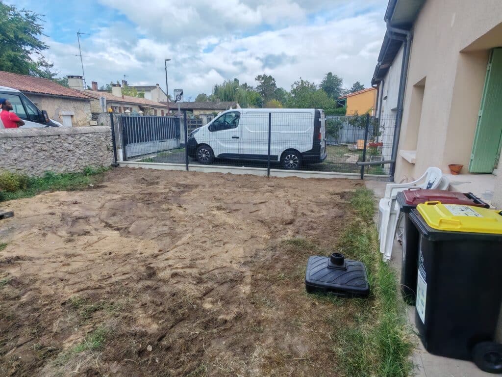 Terrain en terre battue devant un fourgon blanc derrière une clôture, poubelles et maisons de village.