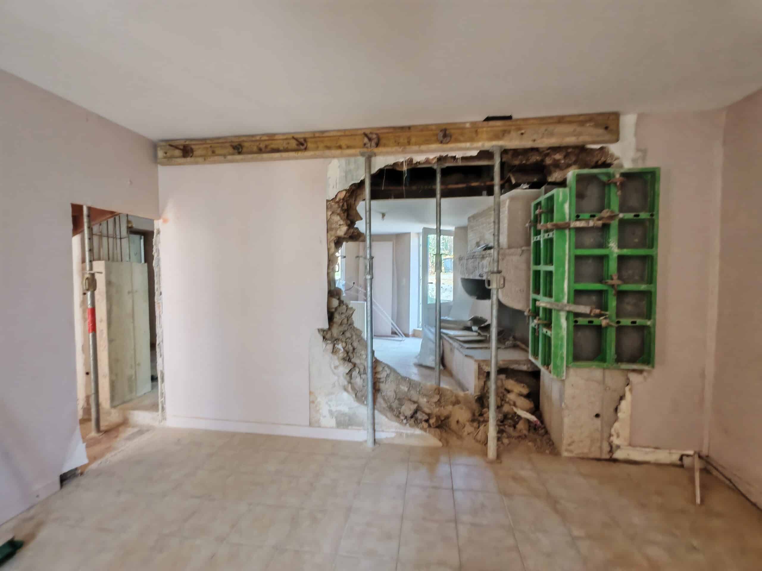 Démolition mur porteur et étaiement pour rénovation Mur démoli avec étais métalliques, poutre bois et coffrage vert dans un intérieur en rénovation.