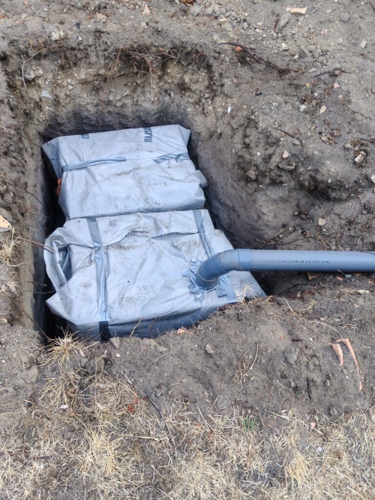 Blocs de drainage enveloppés de géotextile avec raccordement tuyau PVC dans une fosse de jardin.
