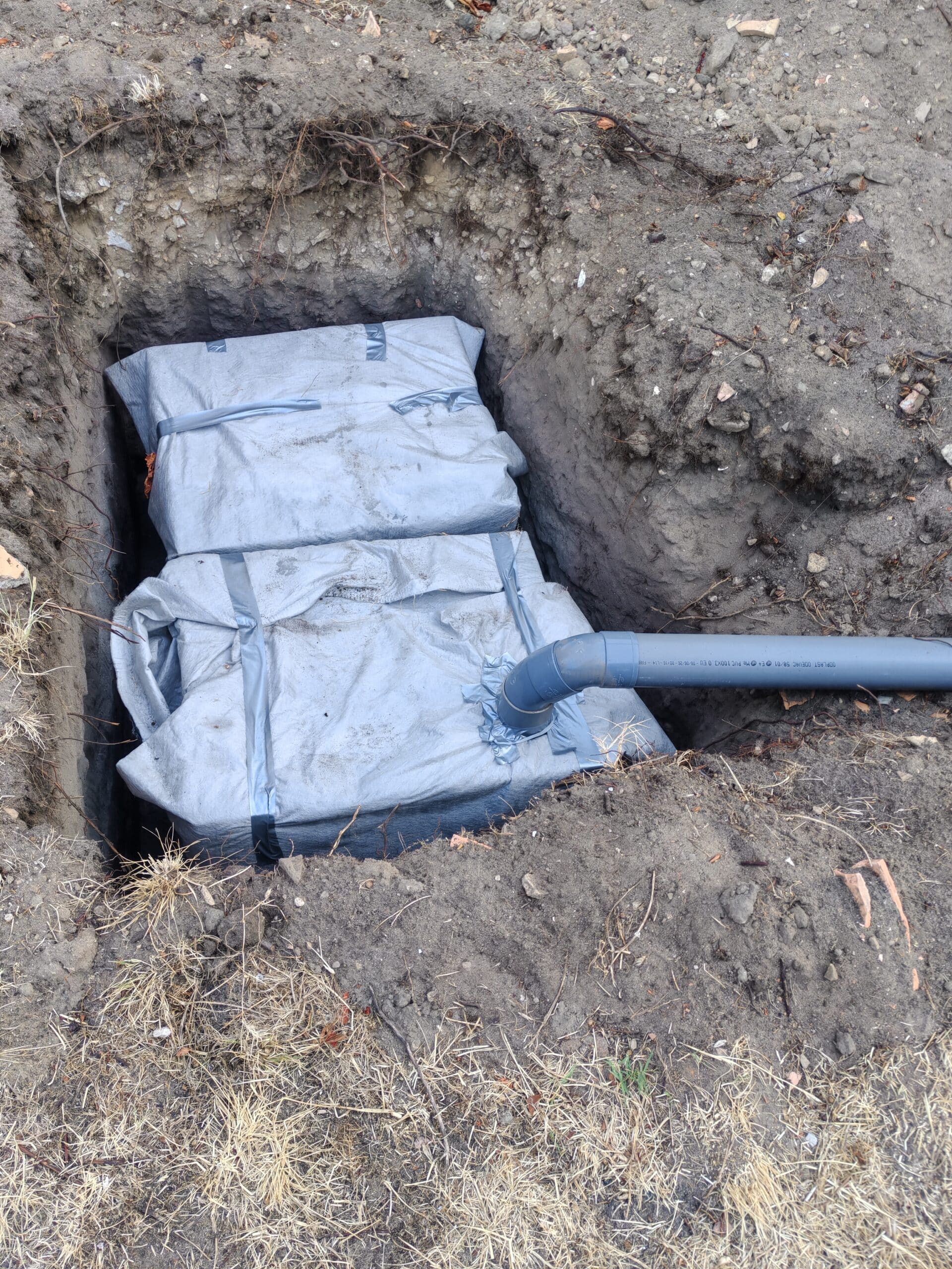 Drainage eaux pluviales : pose de blocs d’infiltration Blocs de drainage enveloppés de géotextile avec raccordement tuyau PVC dans une fosse de jardin.