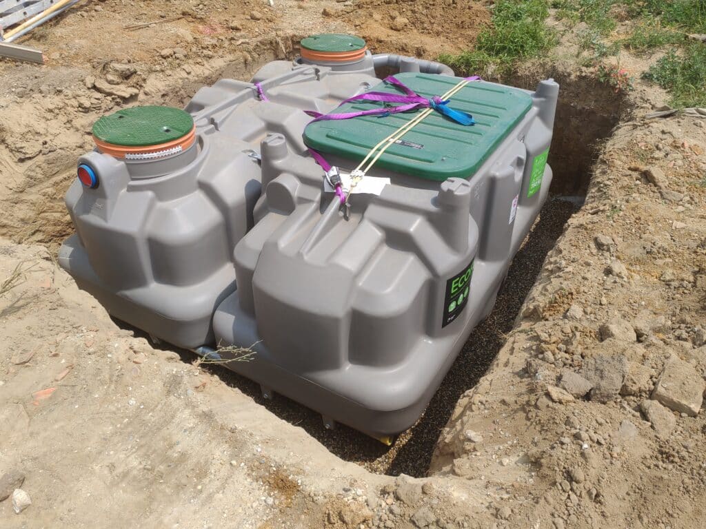 Fosse septique ECO en plastique gris installée dans une tranchée avec couvercles verts.
