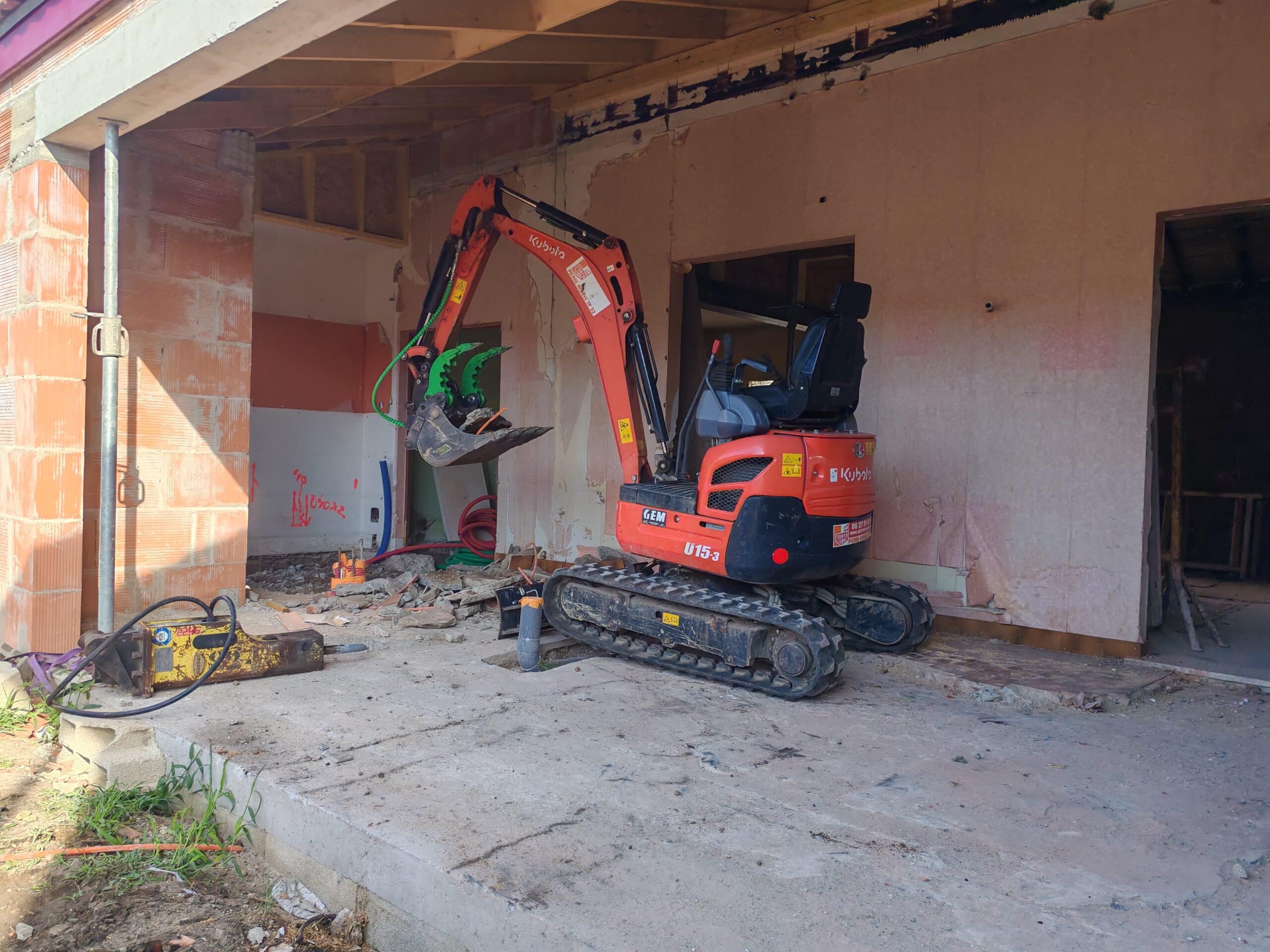 Minipelle Kubota U15-3 : travaux de rénovation et démolition Minipelle Kubota U15-3 orange sur un chantier de rénovation intérieure avec brise-roche hydraulique.